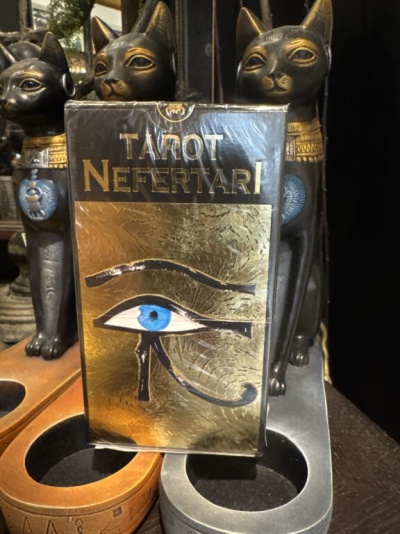 Embalagem do baralho Tarot Nefertari com o Olho de Hórus azul, entre estátuas de gatos e suportes para objetos