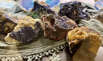 Pedras brutas coloridas em cima de tecido cinza com franjas