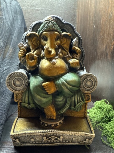 Estátua de Ganesha dourada e verde sentada numa cadeira decorativa