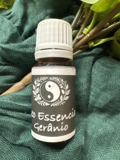 Frasco de óleo essencial de gerânio com etiqueta preta e símbolo yin-yang sobre pano verde