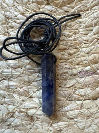 Colar com pendente de cristal azul e cordão preto sobre esteira de palha