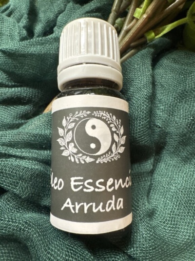 Frasco de óleo essencial Arruda com rótulo preto e símbolo yin-yang em tecido verde.