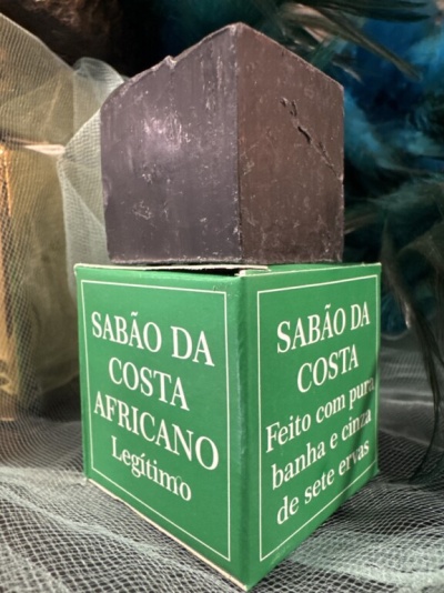 Sabonete castanho escuro em cima de caixa verde com texto branco sobre tecido translúcido