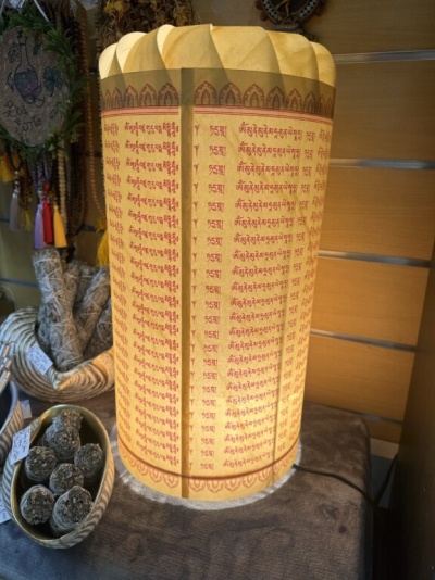 Luminária cilíndrica amarela com texto em tibetano e objetos de decoração ao redor