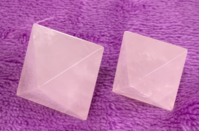 Dois cristais rosa em forma de pirâmide sobre tecido roxo