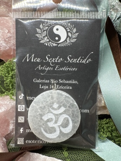 Colar esotérico com pendente branco translúcido e símbolo ॐ em saco plástico com cartão da loja Meu Sexto Sentido
