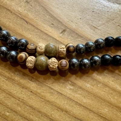 Duas pulseiras com contas de madeira, pedra verde e contas pretas numa superfície de madeira.