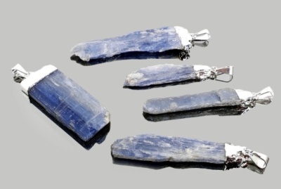 Cinco pendentes de pedra azul kyanite com metal prateado sobre superfície cinzenta refletora