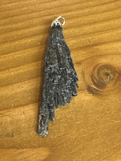Pingente de cristal negro bruto com aro metálico prateado em fundo de madeira clara