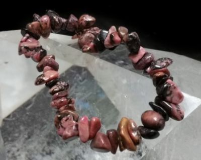 Pulseira de pedras naturais irregulares rosa, preto e castanho sobre superfície translúcida