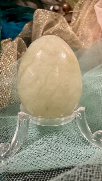 Ovo decorativo de pedra esbranquiçada em suporte transparente sobre tecido dourado e verde