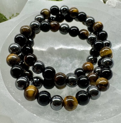 Colar ou pulseira de contas castanhas, pretas e douradas sobre superfície branca