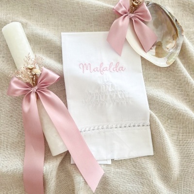 Conjunto com vela, toalha bordada com nome e concha decorada sobre tecido bege claro