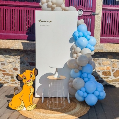 Painel branco com balões azuis e bege, texto 'Lourenço 1º Aniversário' e figura do Simba do Rei Leão em exterior