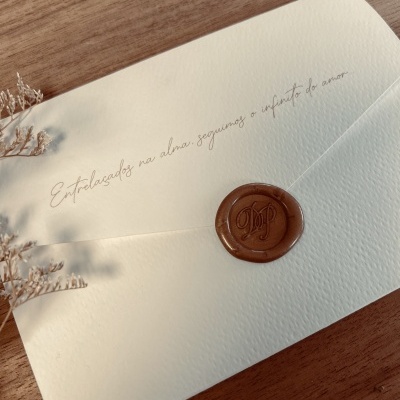 Envelope branco texturizado com selo de cera castanho e texto manuscrito cinza