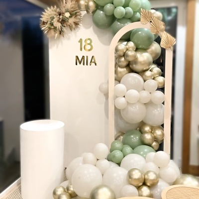 Decoração para festa com balões verdes, brancos e dourados e painel com texto 18 MIA
