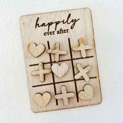 Jogo da velha de madeira com peças em forma de corações e cruzes e texto 'happily ever after'