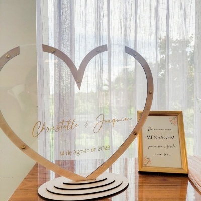 Escultura em acrílico coração com inscrições e quadro com mensagem em português sobre mesa