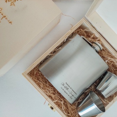 Conjunto de cantil e dois copos metálicos prateados em caixa de madeira com palha