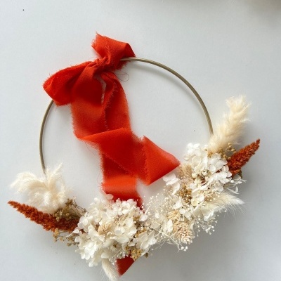 Guirlanda com flores secas e fita vermelha em estrutura metálica dourada