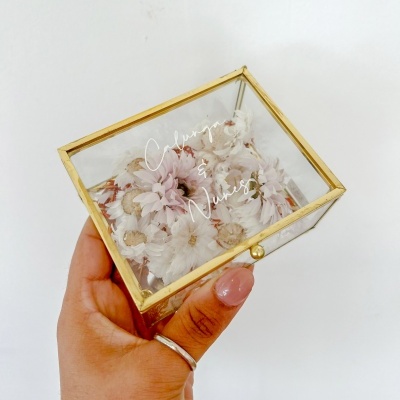 Caixa de vidro dourada com flores secas e texto Colar & Novias, mão feminina a segurá-la