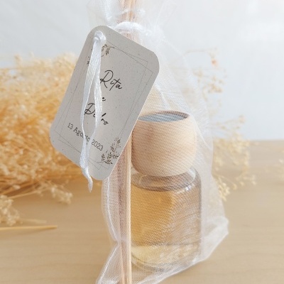 frasco de vidro com tampa de madeira e palitos em saco de tule branco com etiqueta pendurada