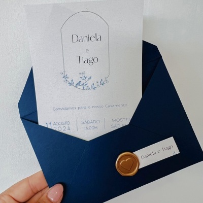 Convite de casamento azul escuro com selo dourado e cartão branco com nomes Daniela e Tiago