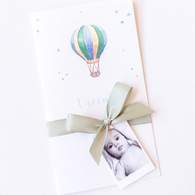 Convite branco com ilustração de balão e laço verde com foto de bebé