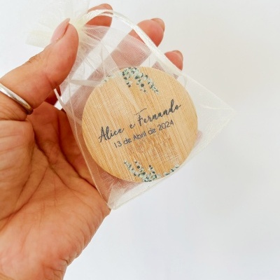 Disco de madeira redondo com texto e elementos florais dentro de saco transparente de organza