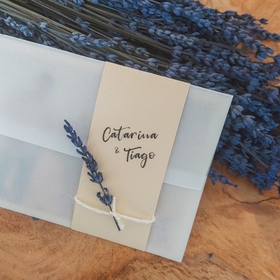 Convite translúcido branco decorado com lavanda e faixa com os nomes Catarina e Tiago.