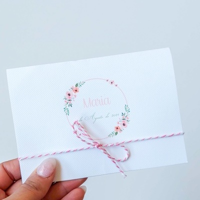 Convite branco com decoração floral e cordão rosa e branco em fundo claro