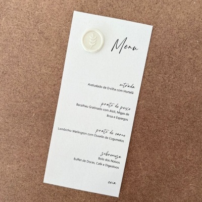 Cardápio em papel branco com texto em português sobre fundo castanho texturizado.