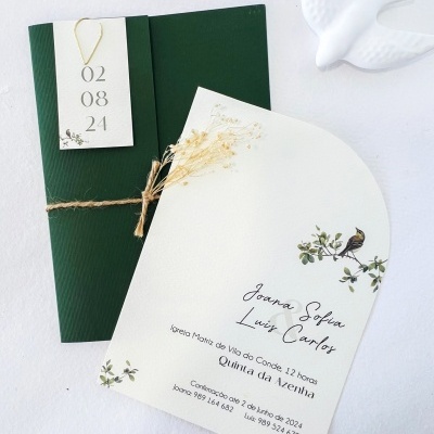 Convite de casamento com envelope verde e decoração de flores secas sobre superfície branca