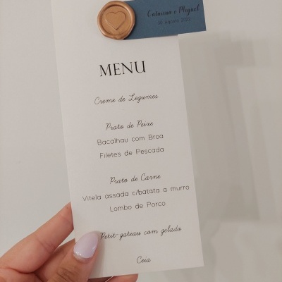 Cartão de menu branco com texto e selo de cera dourado, mão segurando