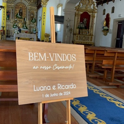 Placa de madeira com texto de boas-vindas ao casamento sobre suporte de madeira dentro de igreja decorada