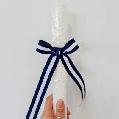 Vela branca decorativa com fita listrada azul e branca segurada por mão