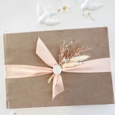 Caixa castanho claro com fita rosa e flores secas, duas aves brancas na parede