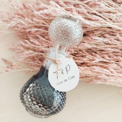 Frasco de vidro com licor de café e ramos secos cor de rosa ao fundo.