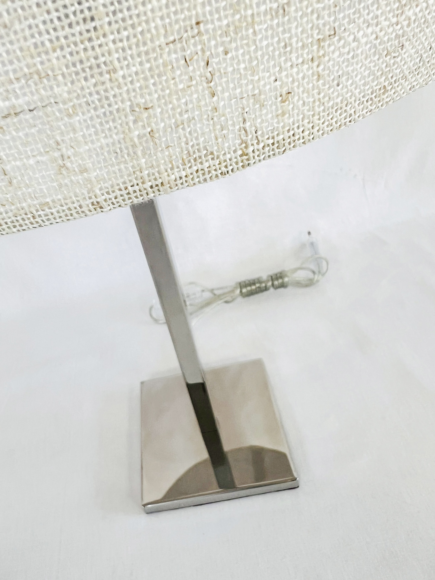 MF004 Lâmpada de mesa com base metálica prateada e cúpula branca de tecido com padrão de malha.