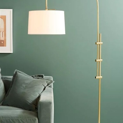 Candeeiro de pé dourado com cúpula branca ao lado de sofá verde em sala com parede verde