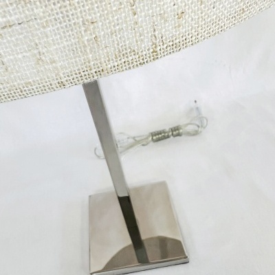 Lâmpada de mesa com base metálica prateada e cúpula branca de tecido com padrão de malha.
