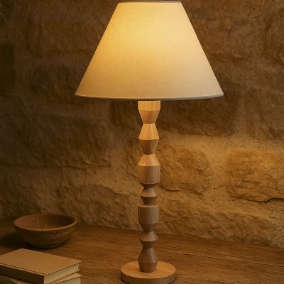 Lâmpada de mesa com base em madeira geométrica e abat-jour bege sobre mesa de madeira rústica com livros e taça