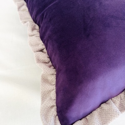 Travesseiro roxo com borda franzida bege sobre superfície branca