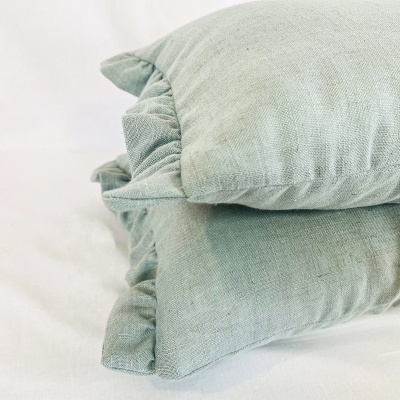Três almofadas verdes-acinzentadas empilhadas com bordas franzidas