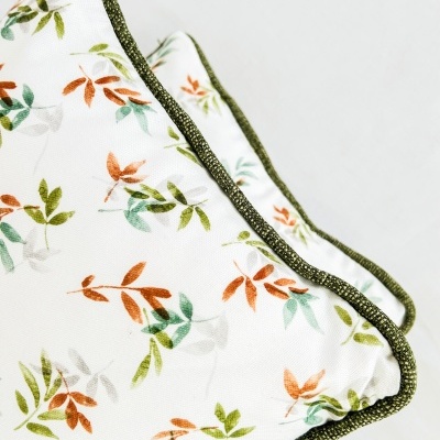 Almofadas brancas com padrão de folhas coloridas e borda verde escura.