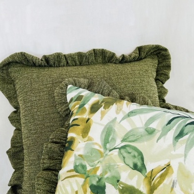 Duas almofadas decorativas, uma verde texturizada e uma com padrão de folhas verdes e amarelas