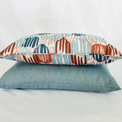Duas almofadas empilhadas, uma com padrão colorido e outra azul esverdeada lisa