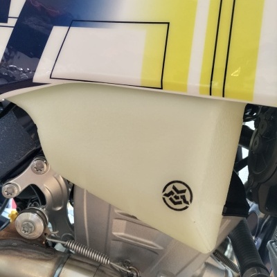 Peça de mota com depósito branco e símbolo preto junto a estrutura metálica