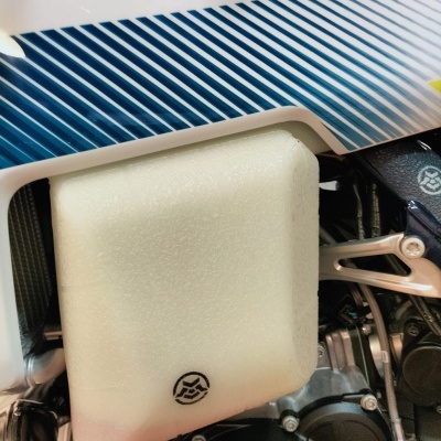 Peça de motocicleta branca com linhas azuis e reservatório translúcido branco em motor preto