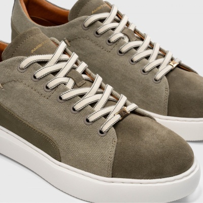 Ténis verde-cinza com sola branca e cadarços brancos em fundo cinza claro